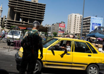 عنصر من قوات اﻷسد يفتش هوية سائق التكسي في دمشق