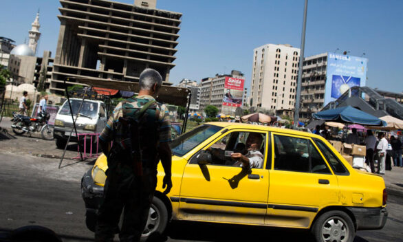 عنصر من قوات اﻷسد يفتش هوية سائق التكسي في دمشق